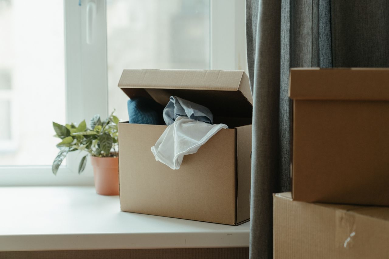 services-08 Open cardboard box with clothes by window, symbolizing moving or relocation.