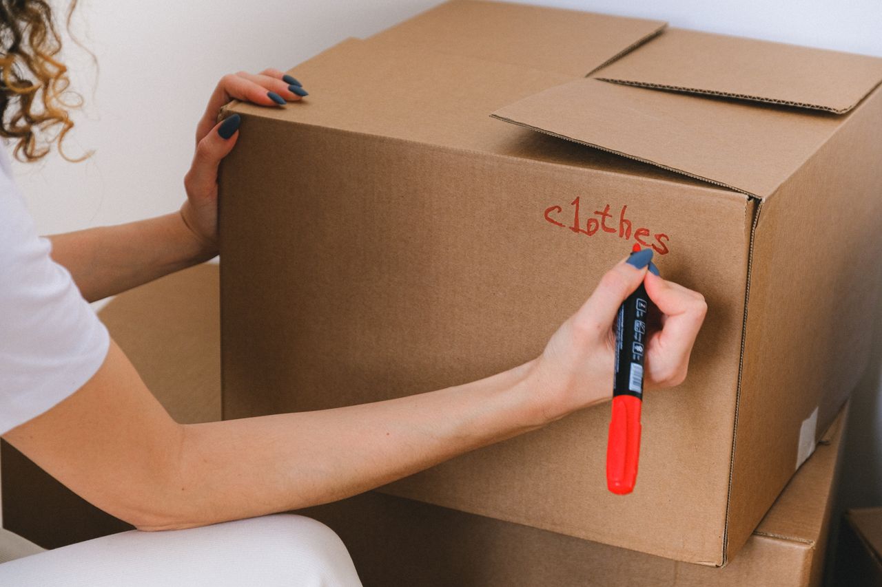 services-07 Close-up of a woman marking a cardboard box with a red marker indoors.