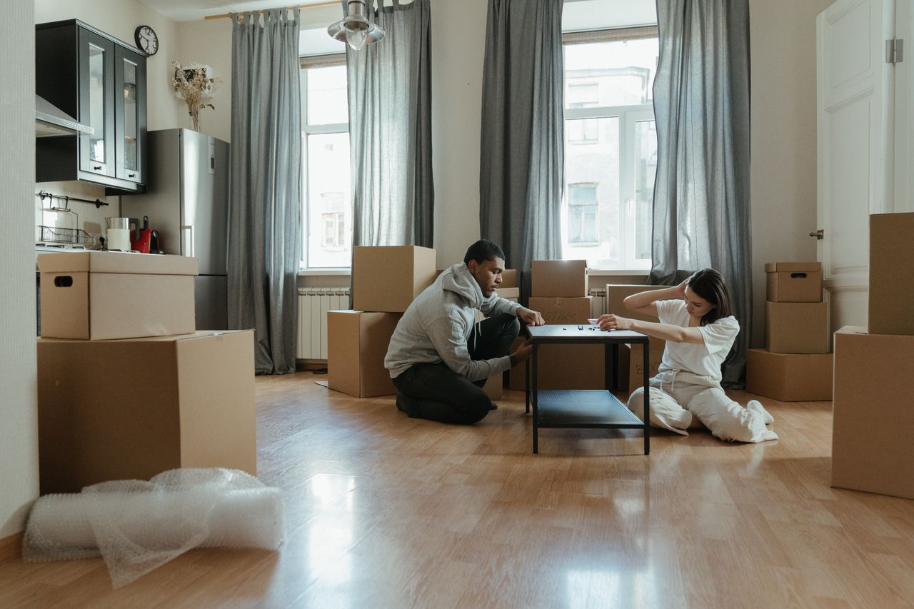 Jeune couple en train de monter des meubles dans leur nouvel appartement, entouré de cartons.